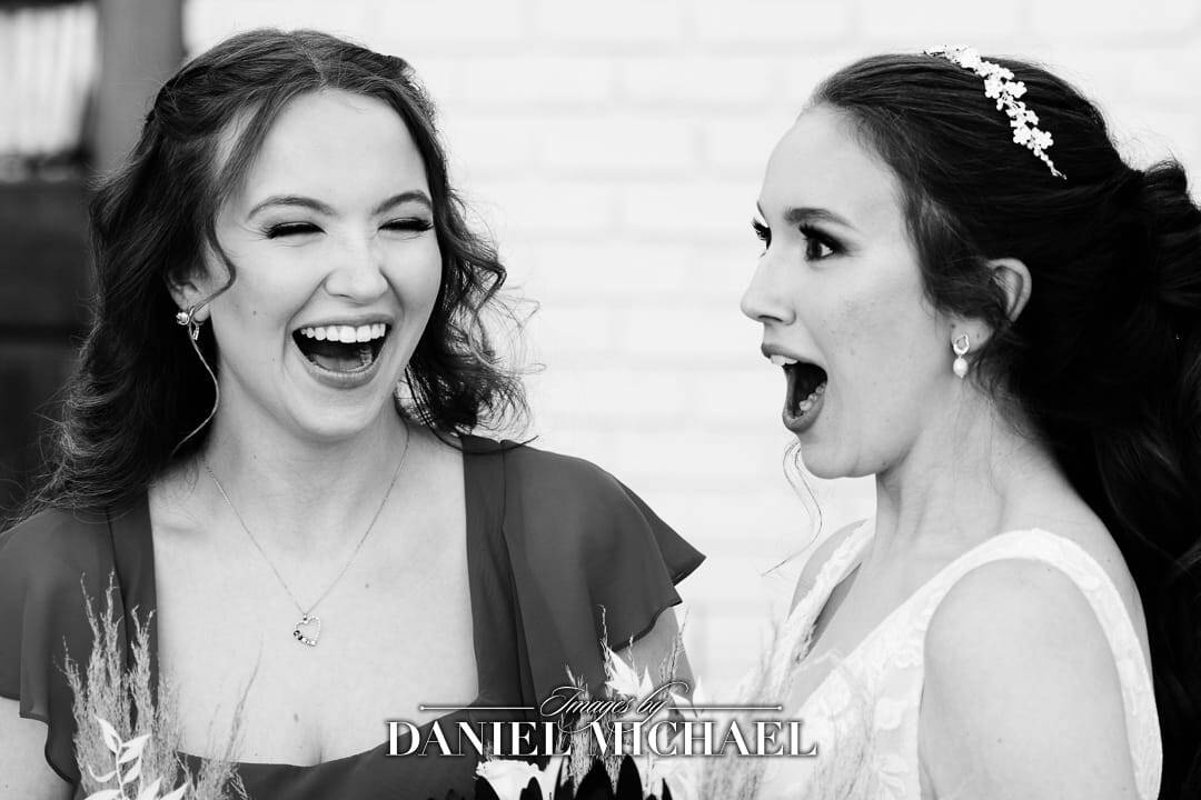 a bride looking surprised next to her laughing sister